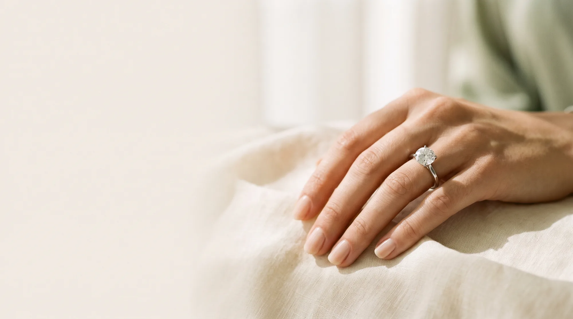 A hand resting on cream linen wearing a platinum solitaire engagement ring